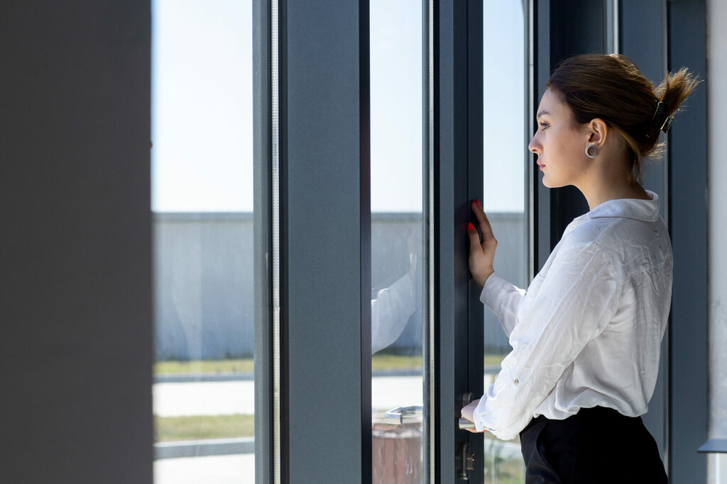 front-view-young-beautiful-lady-white-shirt-black-trousers-looking-distance-through-window-hall-waiting-during-daytime-building-job-activity | GFD Homes Person about to open their doors whilst looking outside.