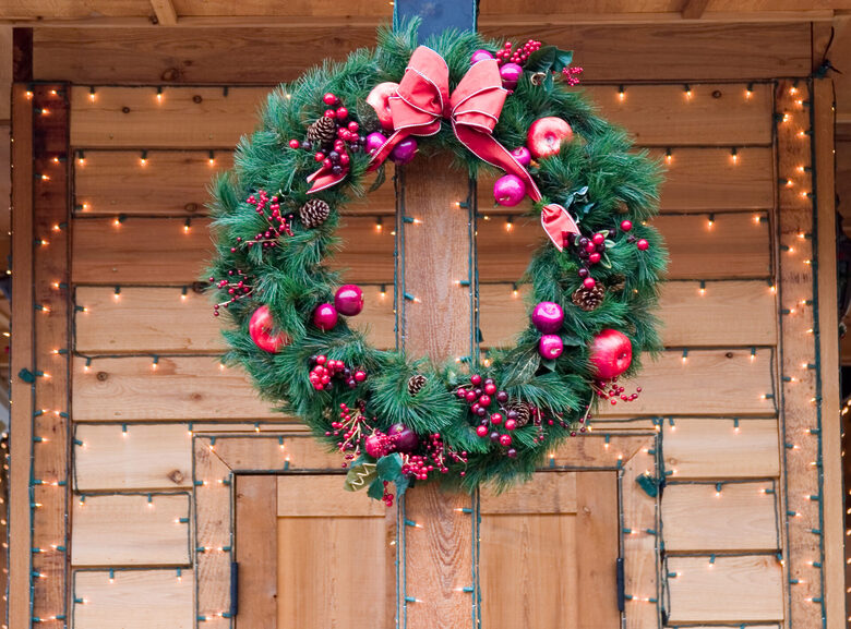 A christams wreath hung on a brown composite door, surrounded by red fairy lights