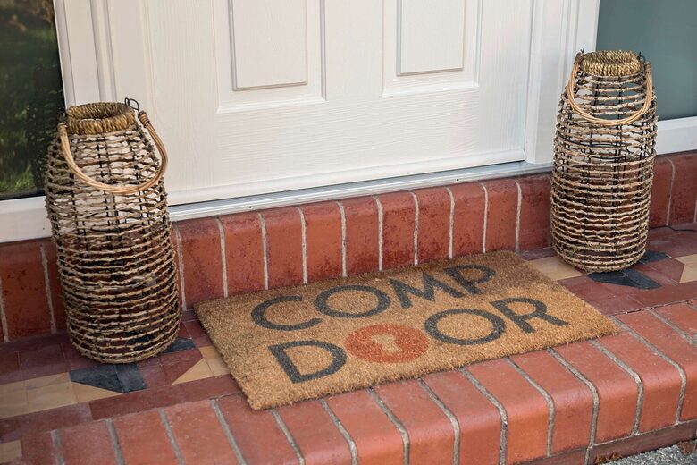 GFD Homes Two tall woven wicker lanterns flank a white front door on a brick stoop, with a coir doormat reading 'WELCOME'.