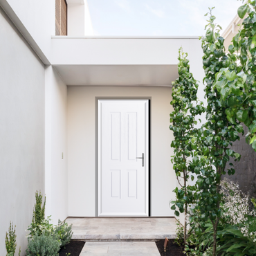 White panel front door in a modern entryway with green shrubs along the right side of the path.